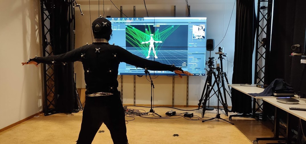 A participant in a motion capture suit in front of a screen with the skeleton model