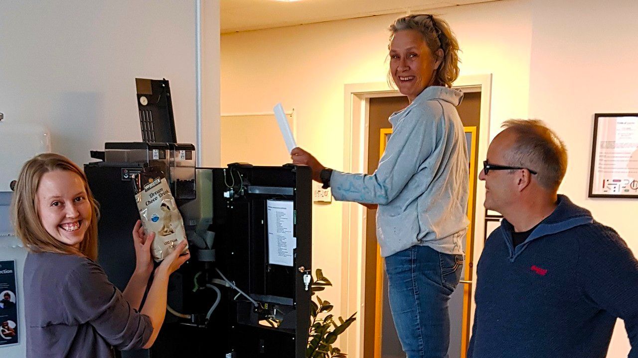 Three colleagues refilling the coffee machine, laughing