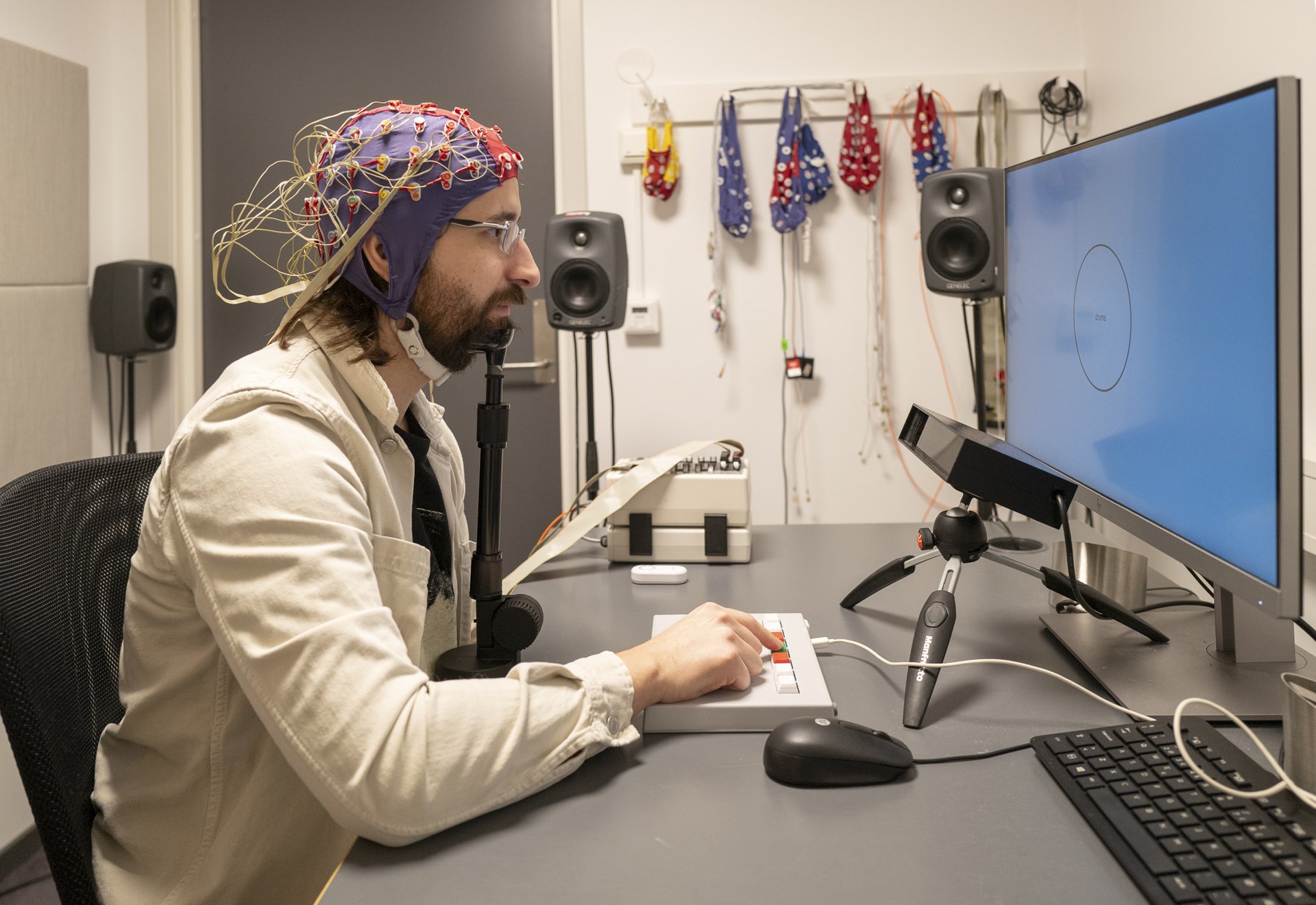 A participant with an EEG cap in front of a screen and an eye tracker