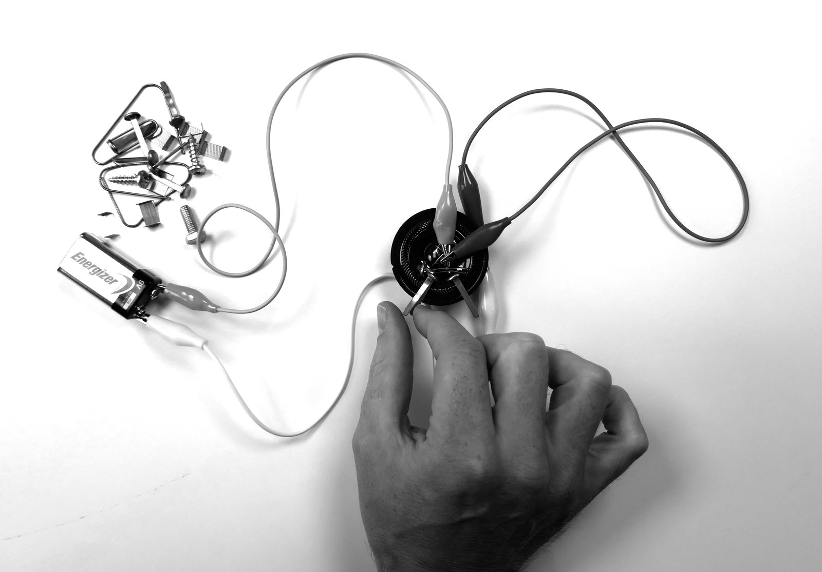A Victorian synthesizer: a 9 V battery, a loudspeaker element, cables with crocodile clips, and a pile of paper clips and screws